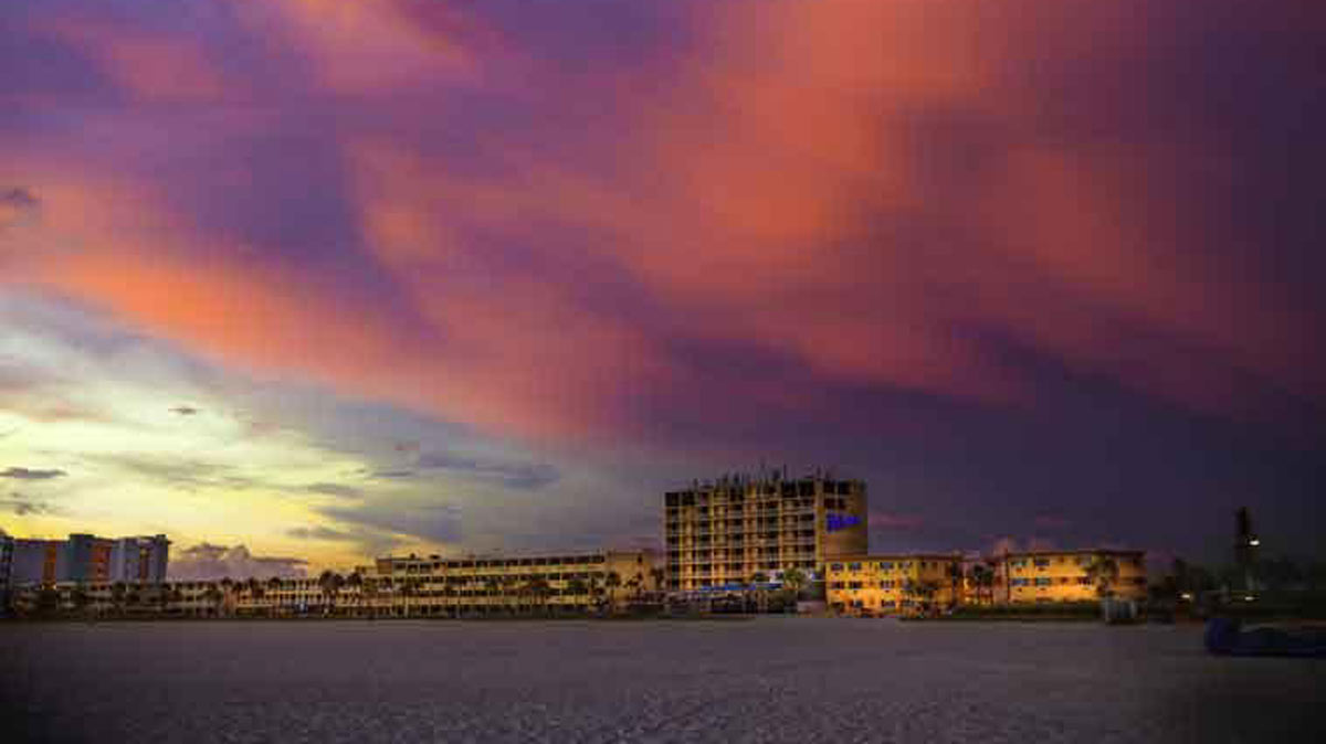 A wide exterior view of a hotel on the beach at sunset.